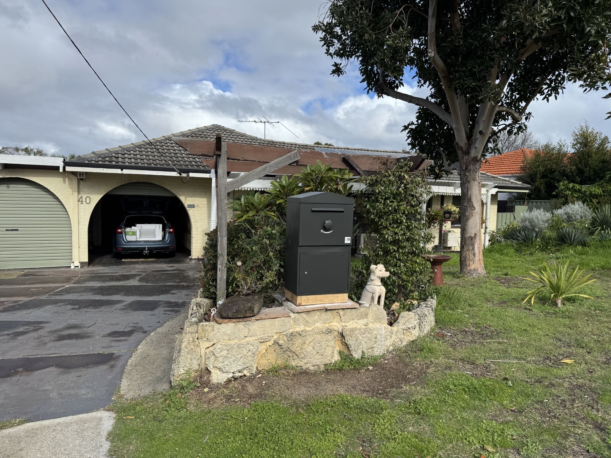 A Large parcel box in Charcoal with a pitched roof, base-mounted on a low limestone retaining wall at a home in Karrinyup, WA, with front parcel collection.